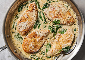 Chicken Florentine in a metal pan, 4 chicken breasts in a cream sauce with cheese and spinach. On a gray countertop.