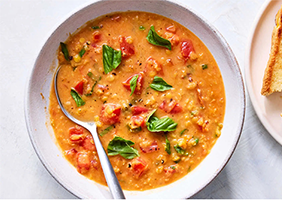 Bowl of Creamy Tomato Lentil Soup, with a spoon in it and a plate of a toasted sandwich to the side.