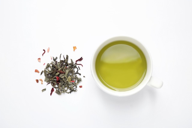 Overhead view of a cup of green tea with tea leaves to the side