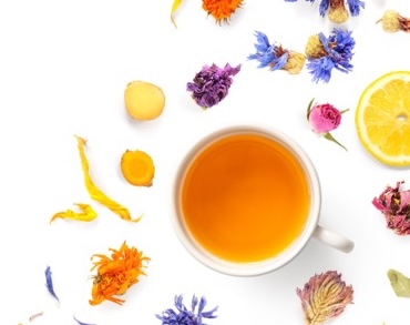 Overhead view of a cup of herbal tea with flowers and herbs to the side