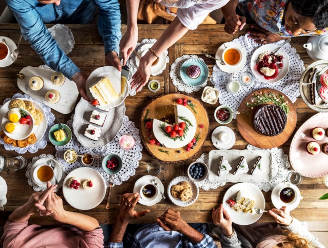 An overhead view of a table set with tea cups,food, and hands reaching