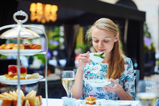 girl sipping out of a tea cup next to a tower of food